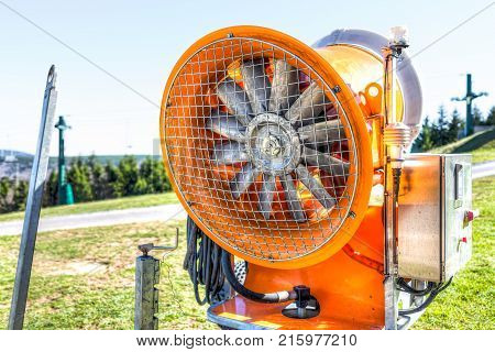 Closeup Of Orange Snow Maker Machine With Fan Blades Near Ski Resort Slope In Autumn, Fall