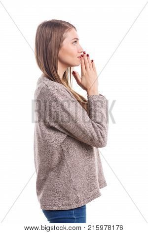 A young brunette girl of European appearance stands sidewise folding her hands together at the level of her chin and prays. Isolated on white background.