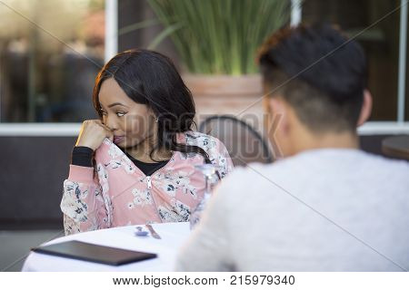 Black female disinterested with a blind date at an outdoor restaurant. They are sitting and chatting like speed dating. The image depicts relationship problems.