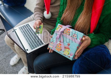 Close-up of a young couple on the couch, a man is holding a credit card and a laptop, a gift girl, online shopping.