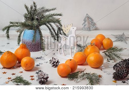 Still life with mandarins, sprigs of spruce in a ceramic vase on a white background Christmas toy with a wooden deer.