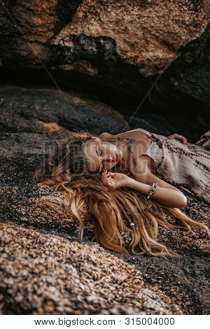 Beautiful Young Boho Style Woman Lying On Stones At Sunset