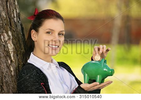 Saving During Sunny Days So When The Rainy Ones Come. Beautiful Young Female Student Leaning On A Tr