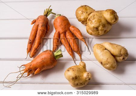 Flat Lay Some Ugly Curved Ogranic Carrots And Potatoes On White Wooden Background.