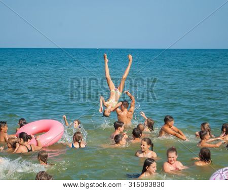 Odesa Rgn. Ukraine, July 29, 2018: A Young Man Throws Up A Girl In The Sea, And She Jumps Into The W