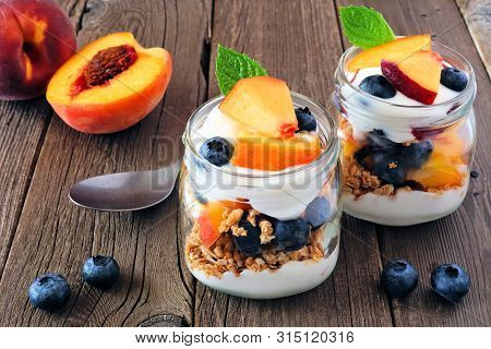 Healthy Peach And Blueberry Parfaits In Mason Jars Against A Rustic Wood Background