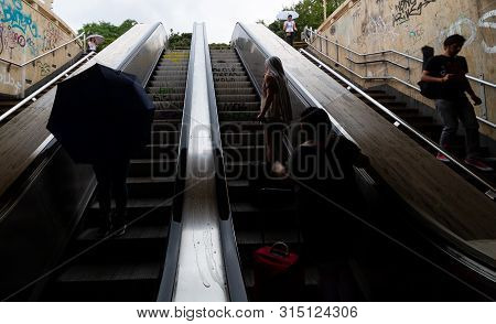 Bucharest, Romania - July 29, 2019: People With Rain Umbrellas Opened Go Up And Down The Escalators 