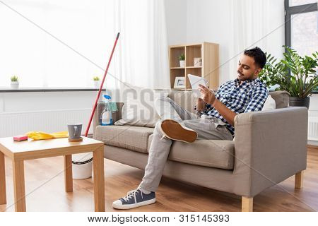 household and time management concept - indian man making to do list in notebook after home cleaning