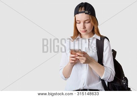 Horizontal Shot Of Beautiful Teenager With Visor Cap Back, Wears White Blouse, Holding Black Backpac