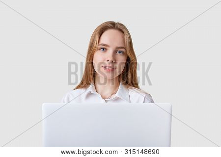 Photo Of Young Caucasian Cheerful Woman Sitting Over White Wall With Lportable Aptop Computer. Looki