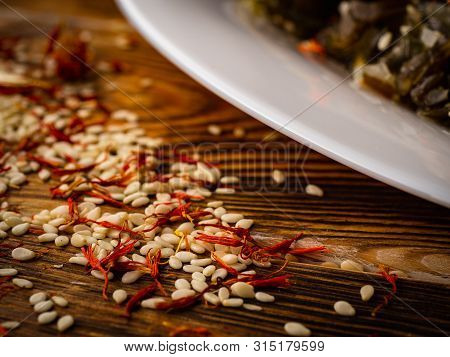 Rosemary And Sesame Spices Near White Plate On Wooden Background.