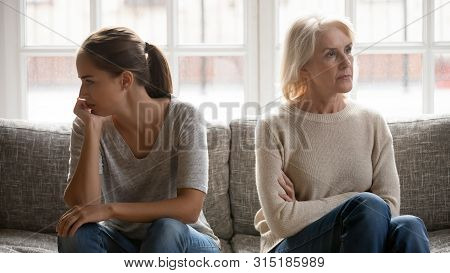 Elderly Mother And Grown Up Daughter Sit On Couch Separately