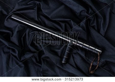 Black Rubber Police Baton On Black Shirt Wrinkled Cloth Low-key Flat Lay