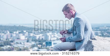 Concept: Working Anytime And Anywhere. Young Handsome Successful Man Is Sitting On The Stone And Wor