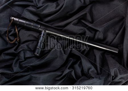 Black Rubber Police Baton On Black Shirt Wrinkled Cloth Low-key Flat Lay