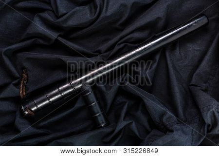 Black Rubber Police Baton On Black Shirt Wrinkled Cloth Low-key Flat Lay
