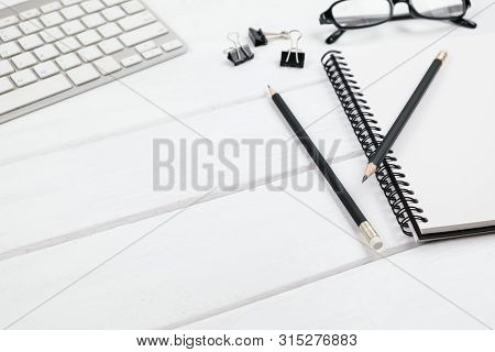 Selective Focus On A Black Pencil On The Sprial Notebook With Paper Clips And White Keyboard On Whit