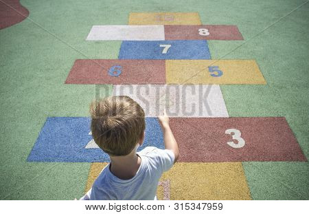Boy Learning Numbers At Rubber Hopscotch. Numbers On The Pavement. Early Education At Mathematics An