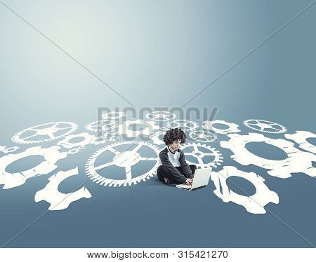 Businessman Working On Laptop And Sitting On A Drawing With Engine Gear Wheels