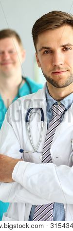 Portrait Of Handsome Man In White Uniform With Stethoscope. Smiling Doc Posing At Workplace In Clini