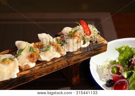 Dumplings With Potatoes And Greaves In Sour Cream On A Wooden Board And Salad. Dumplings With Potato