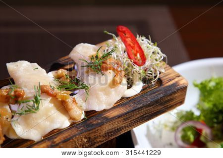 Dumplings With Potatoes And Greaves In Sour Cream On A Wooden Board And Salad. Dumplings With Potato