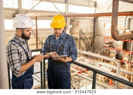 Two young engineers of large factory discussing online technical data