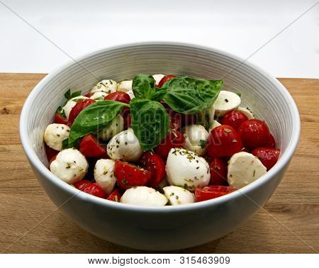 Mozzarella And Tomatoes In White Bowl. Wooden Table, White Background