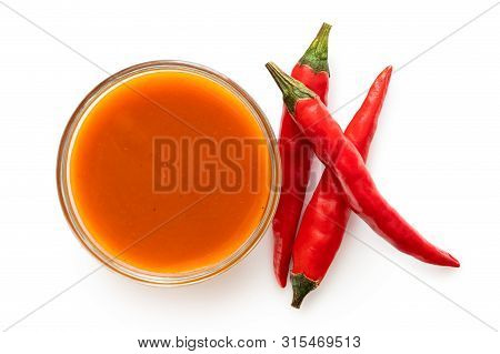 Peri Peri Chilli Sauce In A Glass Bowl Next To Three Red Chillies Isolated On White From Above.