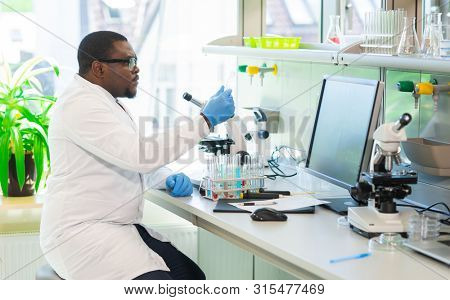 African-american scientist working in lab. Doctor making microbiology research. Laboratory tools: microscope, test tubes, equipment. Biotechnology, chemistry, bacteriology, virology and health care.