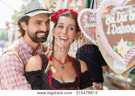 Couple in proper Tracht buying gingerbread hearts of Bavarian fair