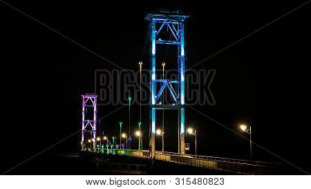 Bridge In A Multi Colored Glow At Night. Pedestrian Bridge In The City Of Zhytomyr Over The River Te
