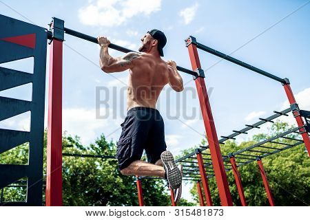 Brutal Athletic Man Making Pull-up Exercises On A Crossbar At Outdoor Streeet Gym.
