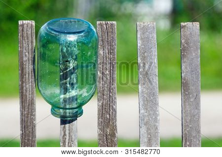 Washed Three Liter Glass Jar Left To Dry Upside Down On Weathered Timber Picket Fence On A Sunny Sum