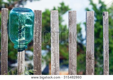 Washed Three Liter Glass Jar Left To Dry Upside Down On Weathered Timber Picket Fence On A Sunny Sum