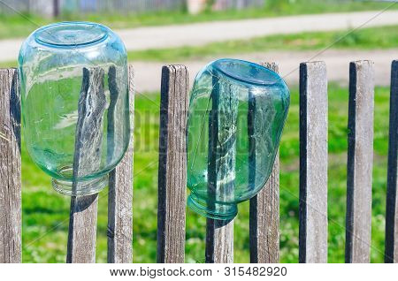 Washed Three Liter Glass Jars Left To Dry Upside Down On Weathered Timber Picket Fence On A Sunny Su