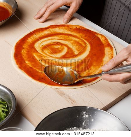 Man Adding Tomato Sauce On Pizza Base, Cooking Italian Meal In Pizzeria, Crop