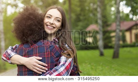 Friendship Contest. Smiling Caucasian Girl Hugging Her Afro Girlfriend In Park, Copy Space