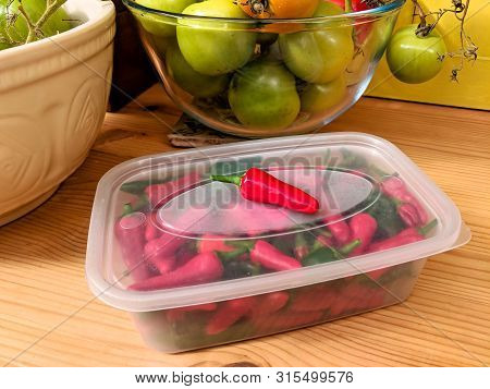 Red And Green Chilli Peppers Stored In A Plastic Container, With An Authentic Kitchen Worktop Backgr
