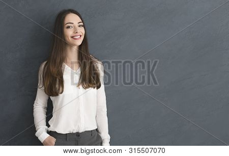 Young Caucasian Girl With One Hand In Pocket, Smiling To Camera, Grey Studio Background With Copy Sp