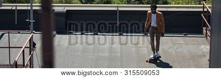 Panoramic Shot Of African American Businessman Riding Lonboard On Rooftop