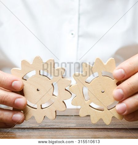 Businessman In White Shirt Connects Two Wooden Gears. Improving Work Efficiency, Establishing New Co