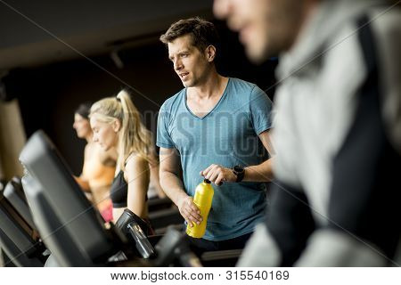 Young Man Drinking Bottle Of Water On Threadmill In Gym