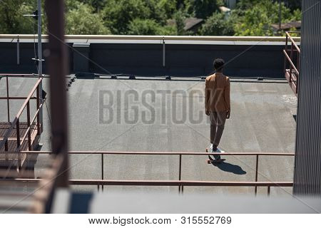 Back View Of African American Businessman Lonboarding On Sunny Rooftop