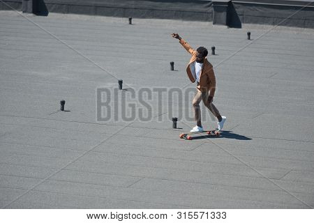 Stylish African American Businessman Riding Lonboard On Sunny Rooftop
