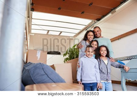 Portrait Of Family Standing On Tailgate Of Removal Truck Outside New Home