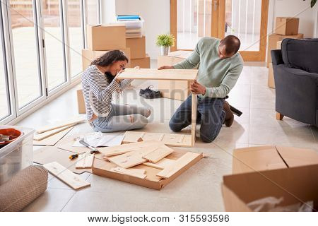 Couple In New Home On Moving Day Putting Together Self Assembly Furniture