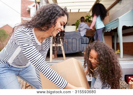 Mother And Children Unloading Furniture From Removal Truck Into New Home