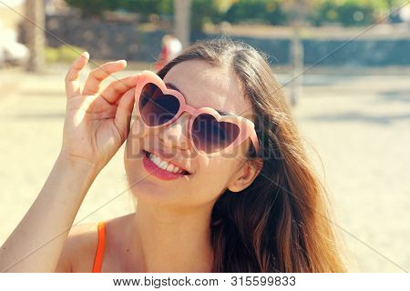 Pretty Brunette Woman In Pink Heart Lolita Sunglasses On The Beach. Holidays, Vacation Travel And Fr