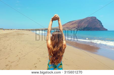 Back View Beautiful Woman Doing Stretching Exercises On The Beach In Playa La Tejita, Tenerife